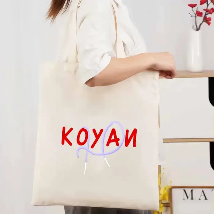 Un sac fourre-tout en toile de couleur crème avec texte Koyani et motifs